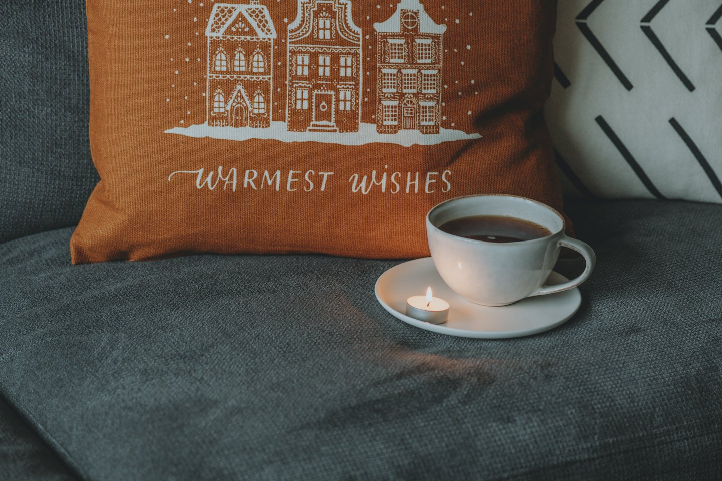 A cup of tea and a candle sit on a sofa.